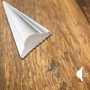 May include: A section of white crown molding with a decorative profile. The molding has a curved bottom edge and a textured, unfinished back. The dimensions are 0.98 inches (2.5 cm) high and 0.43 inches (1.1 cm) thick.