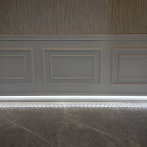 May include: A white wainscoting wall with three panels and a white trim. A thin strip of LED lights is installed along the bottom of the wall, illuminating a gray marble floor.