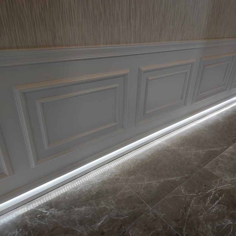 May include: A white wainscoting wall with a recessed LED light strip along the bottom edge. The light illuminates the gray marble floor.