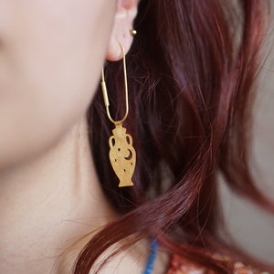 May include: Gold dangle earrings featuring a cutout design of a vase with stars and a crescent moon.