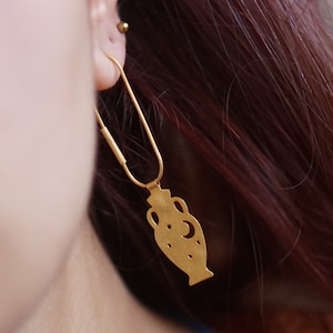 May include: Gold dangle earrings featuring a cutout design of a vase with a crescent moon and stars.