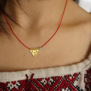 May include: A gold triangle pendant with a turquoise bead on a red cord necklace.