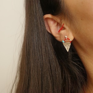 May include: A pair of silver triangle earrings with turquoise beads and red string accents.