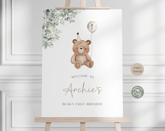May include: A printable welcome sign for a first birthday party. The sign features a brown teddy bear wearing a party hat and holding a balloon with the number 1 on it. The text on the sign reads "Welcome to Archie's Bear-y First Birthday".