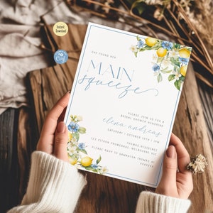 Puede incluir: Una invitación de ducha nupcial azul claro y blanco con un diseño de limón y flores. La invitación dice "She found her main squeeze" e incluye el nombre de la novia, la fecha, la hora y la ubicación.