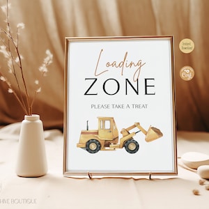 May include: A framed sign with the words "Loading Zone" in a decorative font, and "PLEASE TAKE A TREAT" below. A yellow construction vehicle illustration is at the bottom. The sign is in a gold frame.