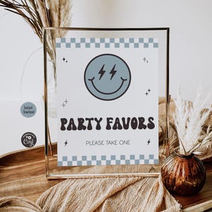 May include: A rectangular sign in a thin gold frame featuring a light blue checkerboard border at the top and bottom. The center displays a light blue smiley face with lightning bolt eyes, the text PARTY FAVORS, and the text PLEASE TAKE ONE.