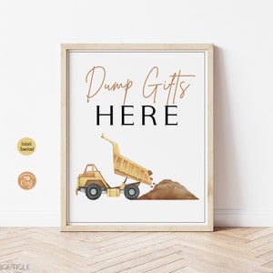 May include: A framed print with the words "Dump Gifts HERE" in gold and black. A yellow watercolor dump truck is dumping brown dirt. The print is in a light wood frame and is on a white background.
