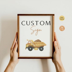 May include: A framed sign with the words "CUSTOM Sign" and a watercolor illustration of a yellow dump truck carrying dirt. The sign has a brown wooden frame and is held by two hands.