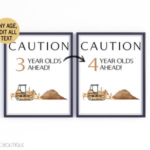 May include: Two framed prints with a construction theme. The prints feature a yellow bulldozer, a pile of dirt, and the text "CAUTION" above "3 YEAR OLDS AHEAD!" and "4 YEAR OLDS AHEAD!". The prints are in a dark blue frame.