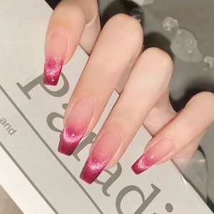 Könnte beinhalten: Ein Set mit fünf langen, mandelförmigen falschen Nägeln mit einem Farbverlauf. Die Nägel sind transparent mit einem rosa-roten Farbverlauf und Glitzerakzenten.