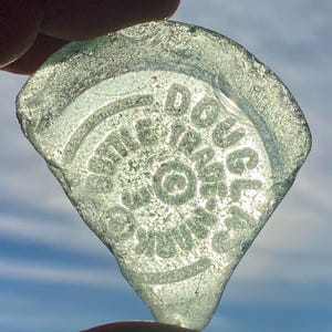 Ljusgrön präglad flaskans framsida ”DOUGLAS Bottle Trade Mark”: Äkta, naturligt, äkta vintage-sjöglas. Ca 5 x 5 cm