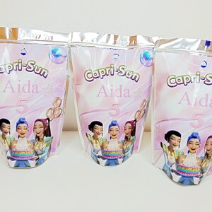 Pode incluir: Três embalagens Capri-Sun com fundo gradiente rosa e branco. Cada embalagem apresenta o texto "Capri-Sun Aida 5" e uma ilustração de mulheres segurando um bolo. As embalagens têm uma parte superior prateada com fecho de correr.