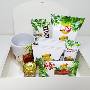 Peut inclure: Une boîte cadeau blanche contenant un mug blanc, un petit pot en verre avec une cuillère à miel en bois et divers paquets de snacks dont Lay's, M&M's, Kinder Country et KitKat. Chaque article présente un motif de feuilles tropicales.