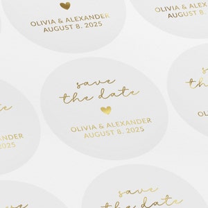 May include: Save the date card with gold lettering on a white background. The card says "save the date" with a small heart and "Olivia & Alexander August 8, 2025".