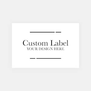 May include: A white rectangular label with the text "Custom Label" in a serif font, with "YOUR DESIGN HERE" below it. Two horizontal black lines are above and below the text.