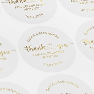 May include: Round, white thank you stickers with gold lettering. The stickers say "Olivia & Alexander" and "Thank you for celebrating with us!" with the date "10.02.2025".