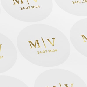 May include: White round stickers with gold lettering. The stickers feature the initials "M/V" and the date "24.07.2024".