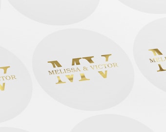 May include: A white circle with a gold foil design that says "Melissa & Victor" with the Roman numeral "IV" on each side of the text.