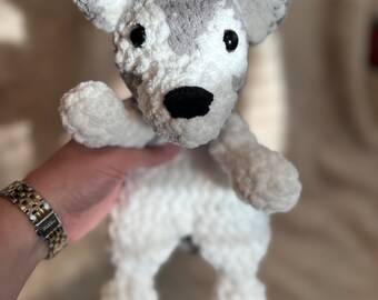 May include: A crocheted stuffed animal dog with white and gray fur, black eyes, and a black nose.