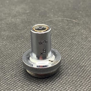 May include: A silver microscope objective lens with a 0.20 inscription and 8x magnification.