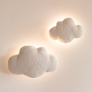 May include: Two fluffy, cloud-shaped wall lights. The lights are a soft, off-white color and have a textured, plush appearance. Each cloud has a warm, glowing light emanating from behind, creating a cozy ambiance.