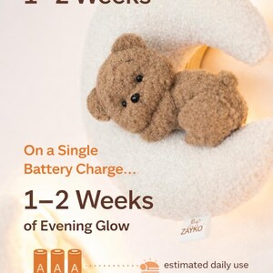 May include: A plush, brown teddy bear rests on a soft, white crescent moon-shaped night light. The image includes text indicating a battery life of 1-2 weeks on a single charge, with estimated daily use.