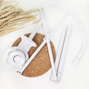 May include: White plastic baby crib mobile parts, including a round base, four arms, and a curved top piece. The parts are laid out on a cork surface.