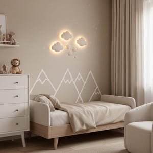 May include: A neutral-toned bedroom with a bed, dresser, and armchair. The wall features a mountain mural and cloud-shaped lights. The bed has a beige blanket and pillows. A rug and curtains complete the cozy space.