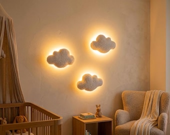 Puede incluir: Tres luces de pared con forma de nube con un brillo cálido están montadas en una pared beige. Las luces están rodeadas de un material suave y texturizado. Una cuna de madera, una silla y una mesa pequeña están en la habitación.