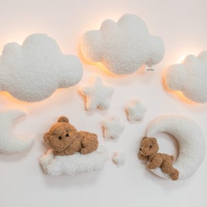 May include: A whimsical nursery wall decor set featuring fluffy white clouds, stars, and a crescent moon. Two brown teddy bears rest on clouds. The set includes a ZAYKO tag.