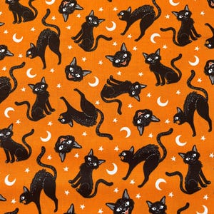 May include: Orange fabric with a repeating pattern of black cats and white crescent moons. The cats are in various poses, some are looking to the side, some are looking up, and some are looking down. There are also white stars scattered throughout the fabric.
