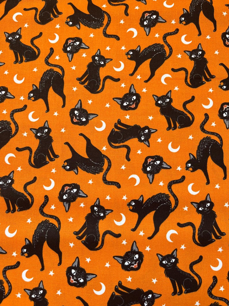 May include: Orange fabric with a repeating pattern of black cats and white crescent moons. The cats are in various poses, some are looking to the side, some are looking up, and some are looking down. There are also white stars scattered throughout the fabric.