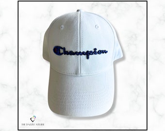 May include: White baseball cap with a blue and white embroidered "Champion" logo.