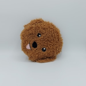May include: A brown plush toy shaped like a dog's head with a pink tongue sticking out and black eyes.