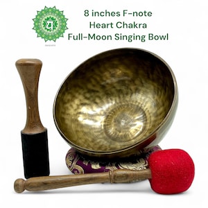May include: A bronze-colored singing bowl, 8 inches in diameter, with a wooden mallet and a striker. The bowl is labeled "Heart Chakra" and "Full-Moon Singing Bowl". The mallet has a black felt end, and the striker has a red felt head.