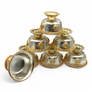 May include: A set of six silver bowls with gold accents. The bowls are stacked in a pyramid shape and have a hammered texture. Each bowl has a raised rim and a small knob on the top.