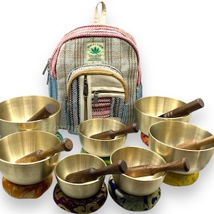 May include: Set of seven singing bowls with wooden strikers, each bowl resting on a colourful cushion. The bowls are arranged in a semi-circle with a hemp backpack in the centre. The backpack has a green leaf logo with the text "Himalaya Hemp Eco-Friendly"