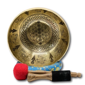 Puede incluir: Un cuenco cantor dorado con diseños intrincados, incluyendo un patrón de flor de la vida, manos y flechas. El cuenco descansa sobre un cojín azul y dorado y viene con dos mazos de madera con cabezales de fieltro rojo y negro.