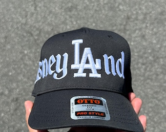 Könnte beinhalten: Schwarze Baseballkappe mit weißer Stickerei, die "sney LA And" lautet. Die Kappe hat ein Etikett mit der Aufschrift "OTTO Classic Fit OSFM Pro Style Maximum Comfort".