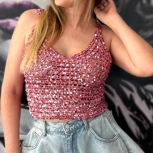 Puede incluir: Un top sin mangas de ganchillo rosa con escote en V y adornos de lentejuelas, combinado con pantalones cortos de mezclilla azul claro con silueta acampanada y dobladillo deshilachado. El texto beautifulcrochetstuff.com es visible.