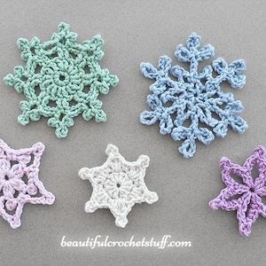 May include: Five crocheted snowflakes in different colours, including white, light blue, light green, and lavender. The snowflakes are arranged on a grey background. The website address "beautifulcrochetstuff.com" is printed below the snowflakes.