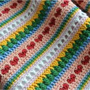 May include: A colourful crocheted blanket with stripes of pink, white, yellow, green, and blue. The blanket has a textured pattern with small hearts and a lacy design.