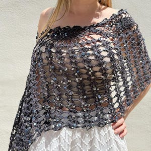 May include: A dark grey crocheted shawl with silver sequins. The open weave design is draped over a white top and skirt. The text "beautifulcrochetstuff.com" is visible at the bottom of the image.