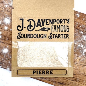 May include: A brown paper packet with a white label that says "J. Davenport's Famous Sourdough Starter Pierre". The packet contains a white sourdough starter.