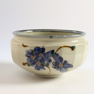May include: A white ceramic bowl with a blue and brown floral design. The bowl has a slightly rounded shape and a wide rim.