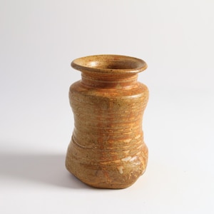 May include: A brown ceramic vase with a textured, speckled finish. The vase has a wide mouth and a rounded base.