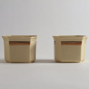May include: Two beige ceramic square planters with brown and orange stripes around the top edge.