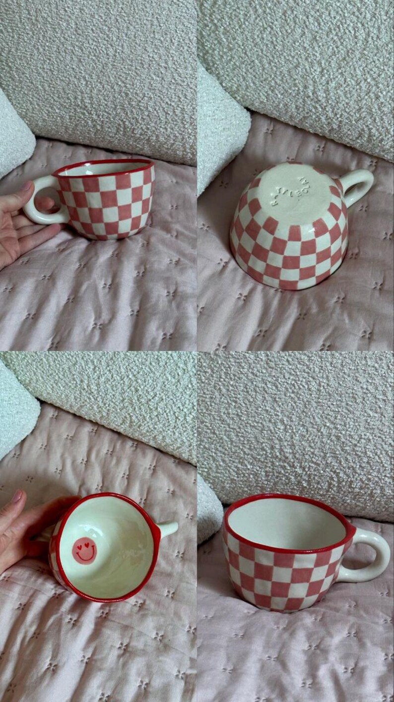 May include: A ceramic mug with a red and white checkered pattern. The rim and handle are red. The interior is white with a small smiley face. The mug is on a pink quilted surface.