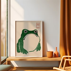 May include: A framed print of a green frog with a white background. The Japanese character "関" is printed in red in the upper right corner of the print.